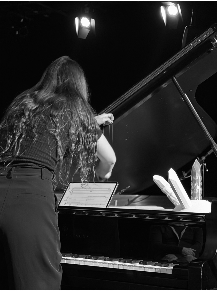 Performer reaching into a grand piano beside the illuminated crystal sculpture used in OUROBOROS